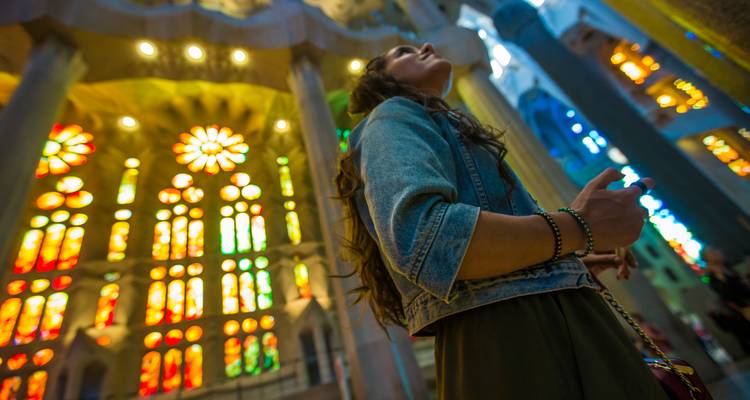 Jonge vrouw die omhoog kijkt naar de kleurrijke glas-in-loodramen in Barcelonas Sagrada Família.