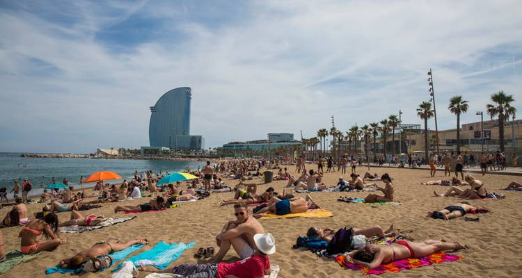 Menigten die zonnebaden en spelen op het Barceloneta-strand van Barcelona met het zeilachtige W Hotel op de achtergrond.