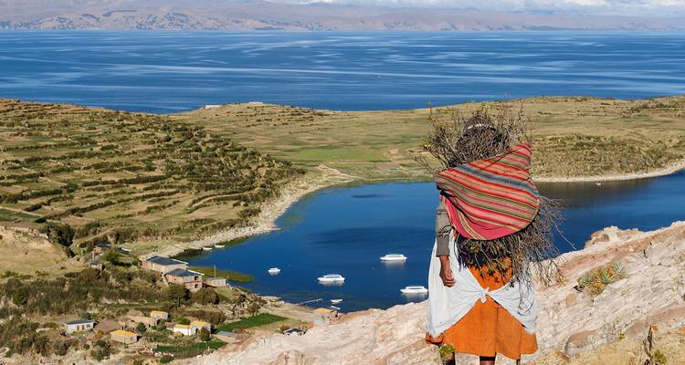 Person mit einem Bündel, die einen See und eine Landschaft betrachtet.