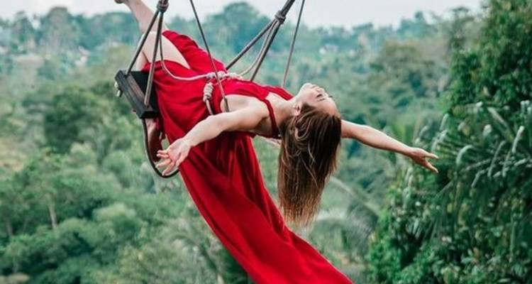 Personne en robe rouge se balançant au-dessus d'un paysage verdoyant luxuriant.