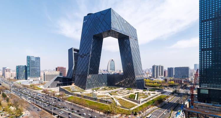 Paysage urbain moderne avec un bâtiment unique et imposant présentant un design en arche, entouré d'autres gratte-ciel et d'une route très fréquentée.