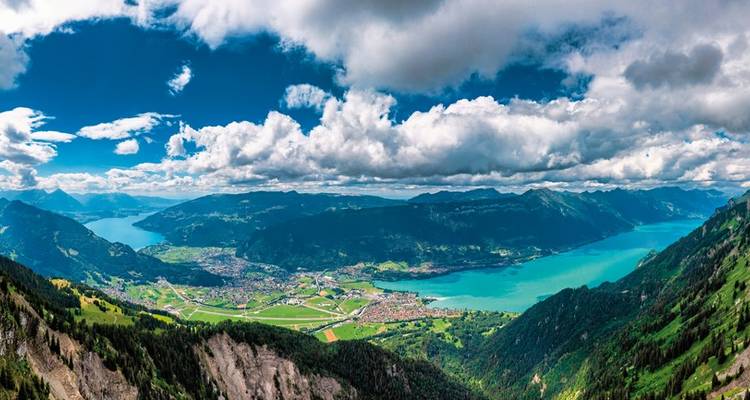 Weite Aussicht auf ein Tal mit einem türkisfarbenen See und Bergen.