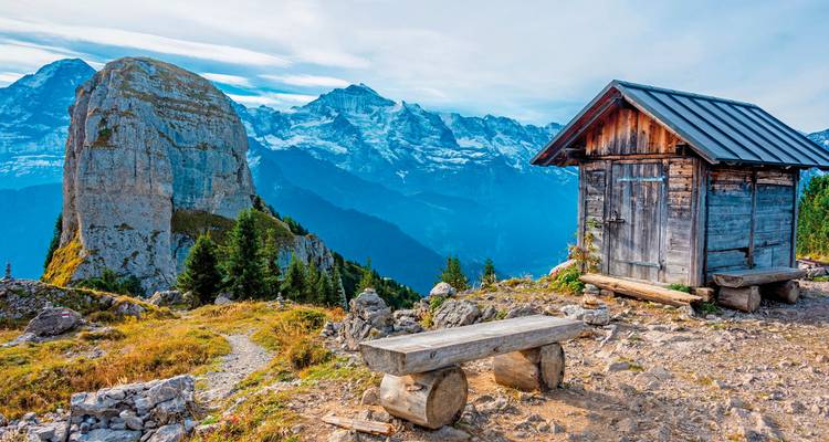 Rustikale Hütte und ein markanter Berggipfel mit Schnee im Hintergrund.