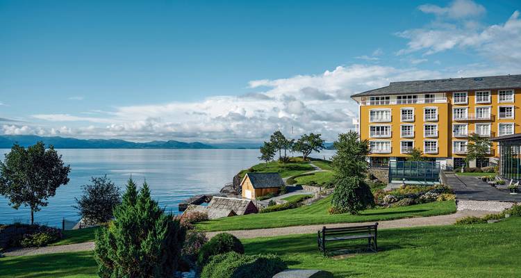 Wunderschöner Blick auf ein gelbes Gebäude am Wasser mit üppigem Grün rundherum.