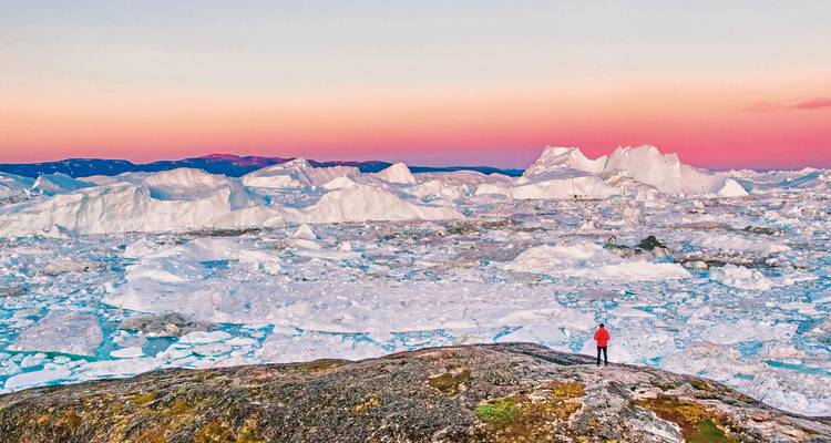 Viajero contemplando un paisaje lleno de formaciones de hielo bajo un cielo colorido.