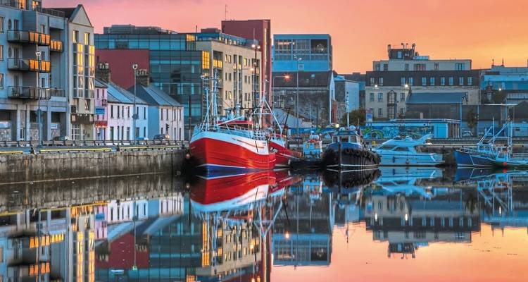 Des bateaux amarrés se reflétant dans l'eau au coucher du soleil dans un port de ville.