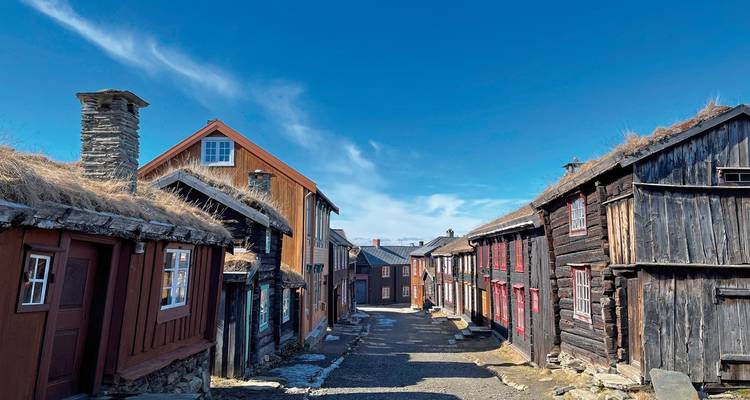 Une rue avec des maisons en bois colorées et un ciel bleu dégagé.