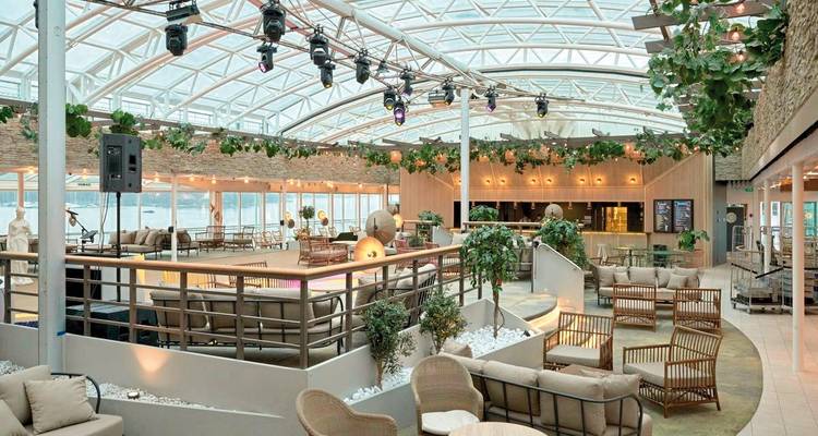 Espace de détente intérieur avec sièges et plantes sous un toit en verre.