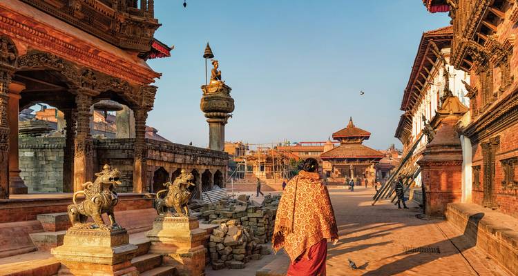 Une personne en tenue traditionnelle marchant à travers une place ancienne avec des temples.