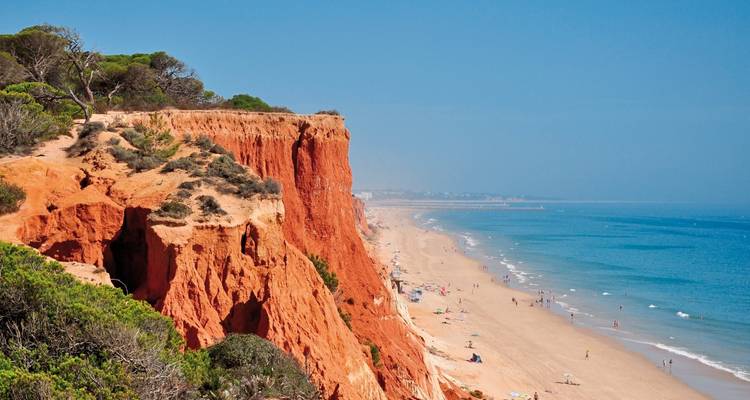 Rote Klippen und ein langer Sandstrand mit dem Ozean.
