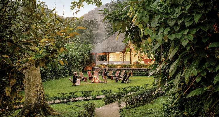 Chaises disposées autour d'un foyer dans un jardin, avec un chalet en arrière-plan.