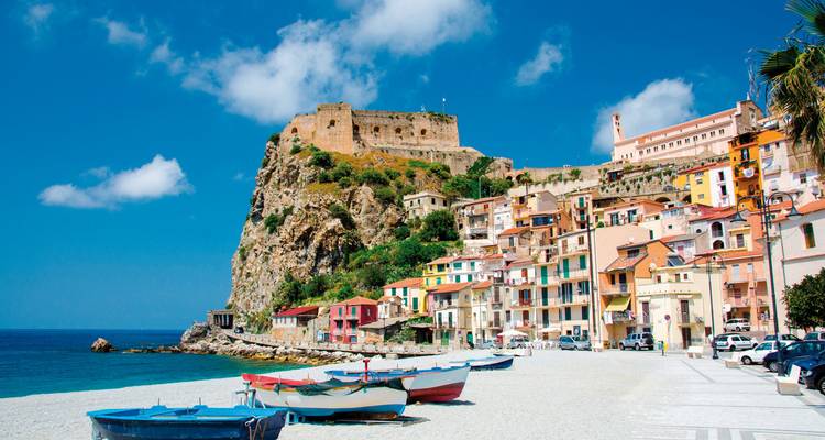 Een schilderachtig kustdorpje met kleurrijke huizen, boten en een fort op de klif onder een heldere blauwe hemel.