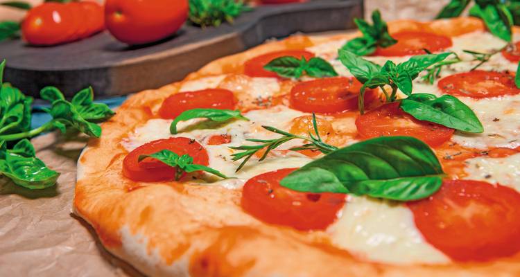 Een vers gemaakte pizza belegd met tomaten, kaas en basilicumblaadjes, geplaatst op een rustieke tafel.