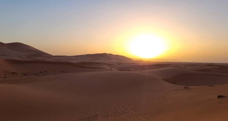 Lever de soleil sur les dunes de sable avec des traces de pneus.