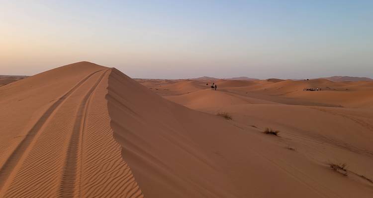Dunes de sable avec des traces de pneus visibles and des collines.