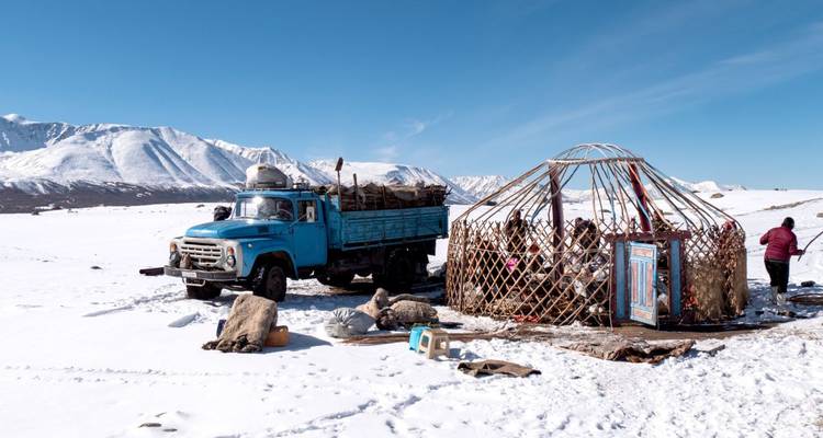 A rugged truck parked near a yurt frame in snowy terrain.