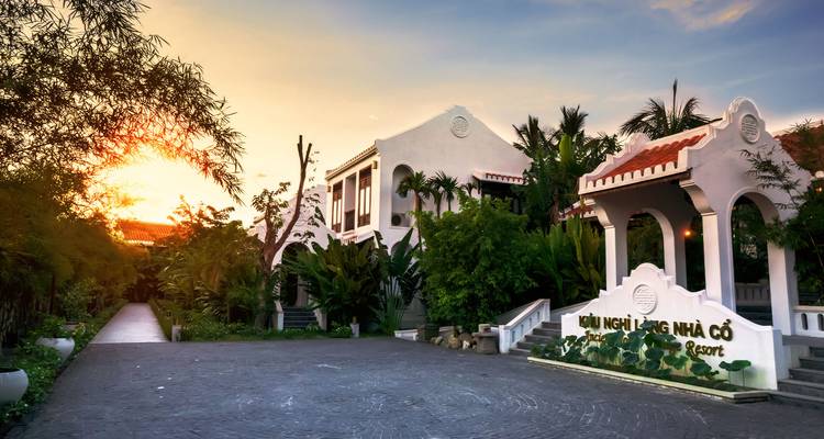 Entrée de complexe hôtelier avec végétation luxuriante au coucher du soleil.