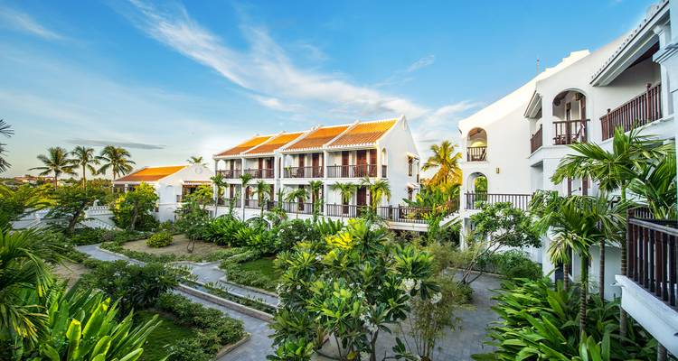 Extérieur d'un complexe hôtelier avec des jardins luxuriants et de grands palmiers.