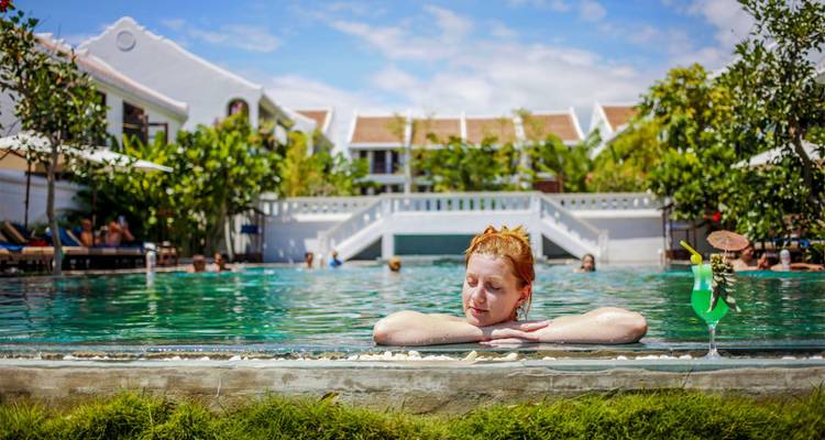 Client se détendant dans la piscine d'un complexe hôtelier avec une boisson.