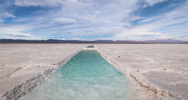 Salt flats with a reflective pool of water leading to distant mountains.