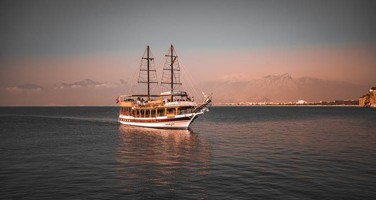 Zeilboot in een kalme zee met bergen op de achtergrond.