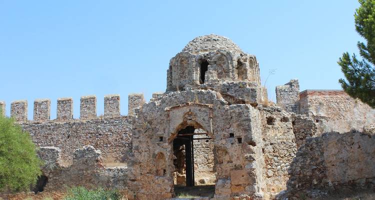 Een oude stenen constructie met bogen en gedeeltelijke ruïnes onder een heldere hemel.