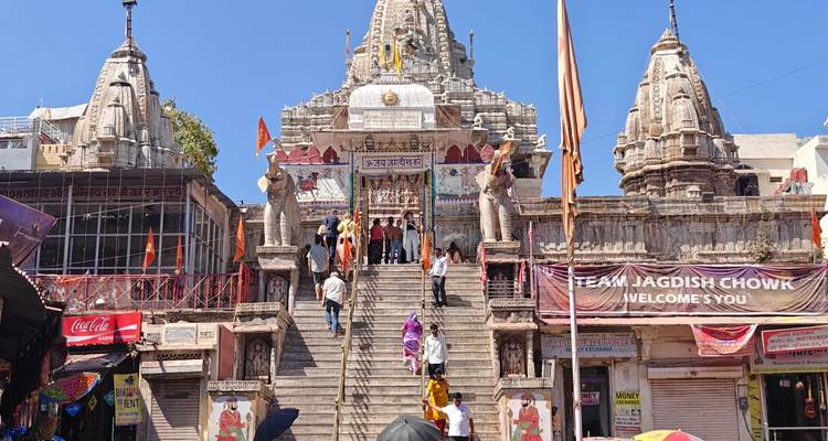 Steile Steintreppe, die hinauf zum Jagdish-Tempel führt, geschmückt mit Elefantenstatuen und leuchtenden Bannern unter einem strahlend blauen Himmel.