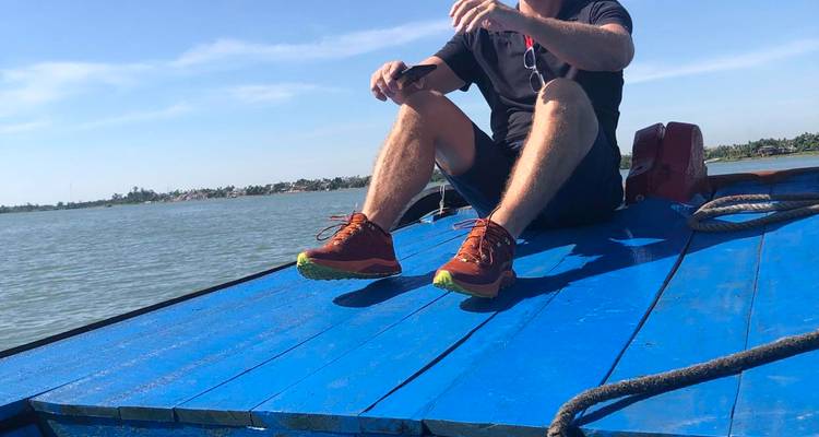 Un voyageur est assis sur le pont bleu vif d'un bateau qui navigue sur une large rivière sous un ciel dégagé.