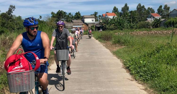 Des cyclistes portant des casques roulent en file indienne le long d'un sentier de béton rural bordé de verdure.