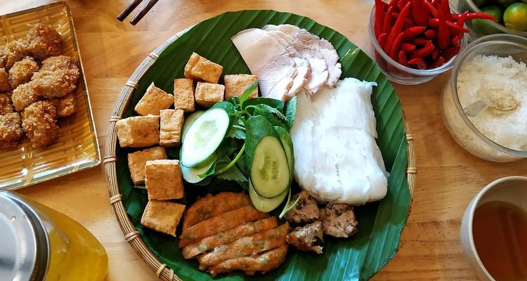 Plateau coloré de plats vietnamiens—porc grillé, tofu, herbes et vermicelles de riz sur feuille de bananier.
