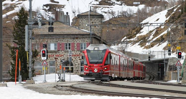 Rode alpine trein die een stenen station binnenrijdt te midden van besneeuwde pieken en seinlichten.