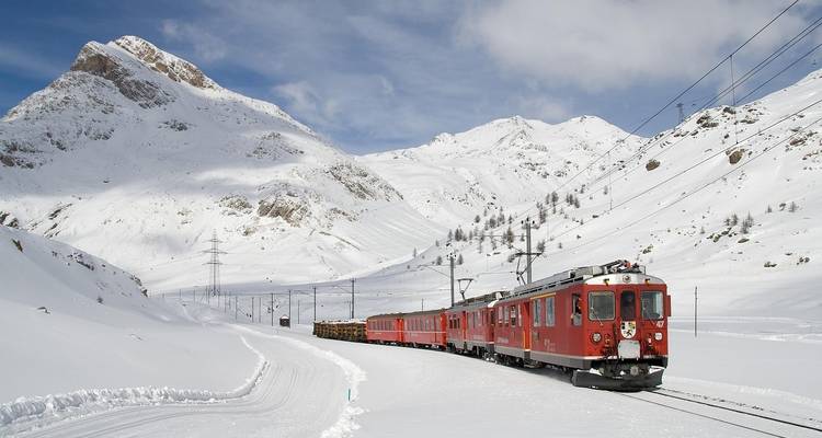 Vintage rode trein die een ongerept wit sneeuwveld oversteekt onder heldere alpenlucht.