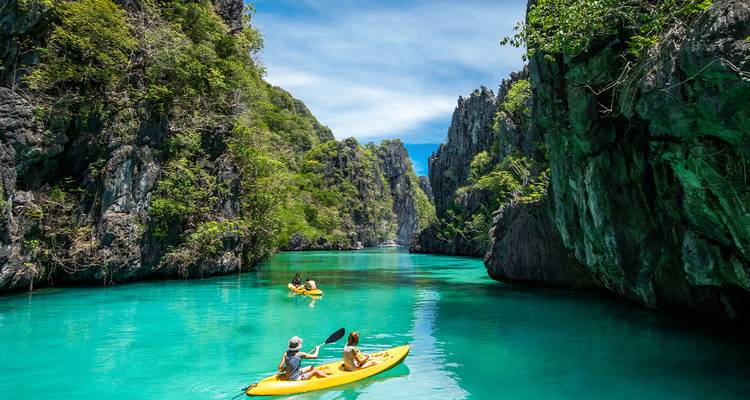 Kayakers paddle through turquoise waters between dramatic limestone cliffs in a tropical lagoon