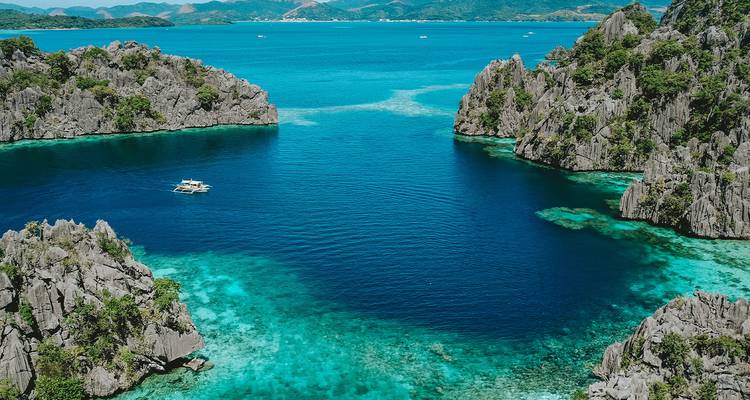 Turquoise lagoon surrounded by jagged limestone cliffs with a lone outrigger boat in the water
