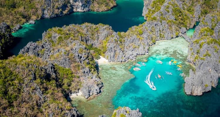 Vista aérea de acantilados de piedra caliza y lagunas turquesas salpicadas de barcas con batangas en un paraíso insular.