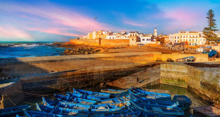 Scenic view of Essaouira harbor with blue boats and colorful sky.