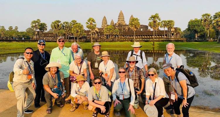 Grupo de turistas posa frente al icónico complejo de templos de Angkor Wat con estanque reflectante.