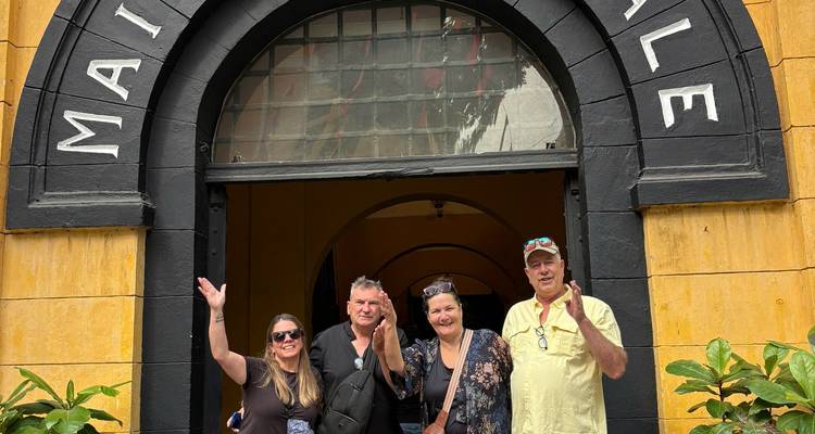 Cuatro viajeros posan alegremente bajo la entrada de arco negro de la histórica prisión Hoa Lo de Hanoi (Maison Centrale).