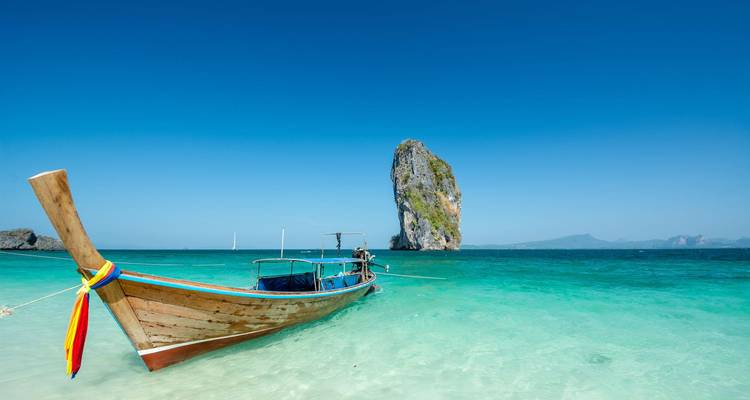Barco tradicional de cola larga flotando en agua turquesa cristalina con una isla de roca caliza al fondo.