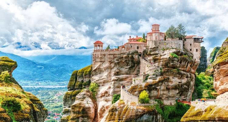 Monastery perched on rock formations under a cloudy sky.