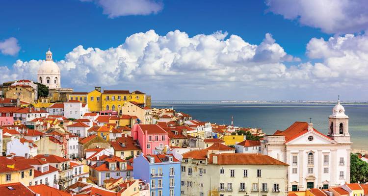 Les maisons colorées du quartier d'Alfama à Lisbonne surplombant l'estuaire du Tage sous des nuages épars.