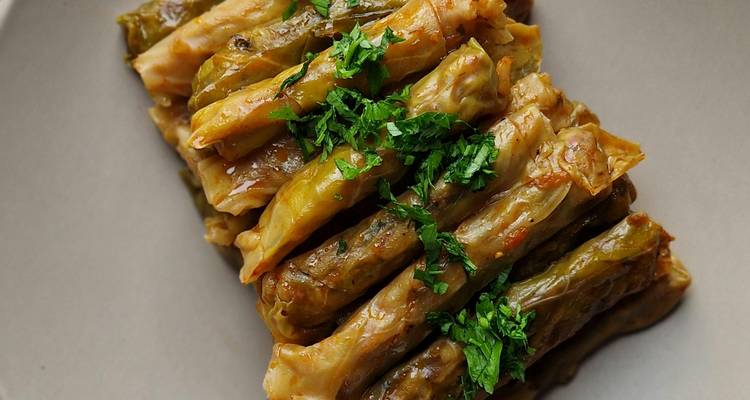 Pila de rollitos rellenos salados garnizados con hierbas picadas, primer plano en un plato neutro.