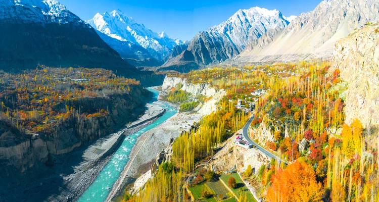 Vaste panorama de la vallée de Hunza avec une rivière turquoise et des arbres dorés d'automne sous des pics enneigés