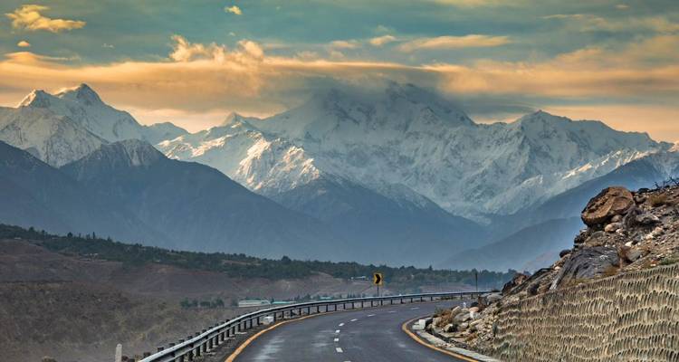 Route sinueuse menant vers les imposantes montagnes enneigées du Karakoram sous des nuages dramatiques