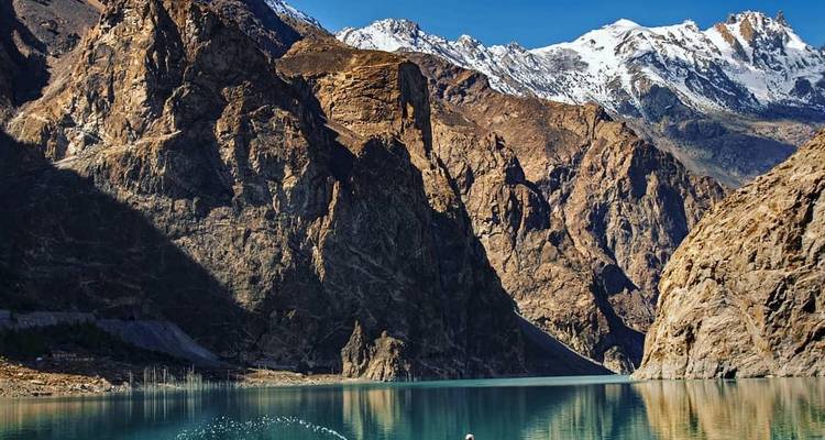 Lac Attabad cristallin entouré de parois rocheuses abruptes et de pics enneigés sous un ciel bleu