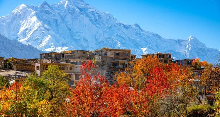 Village traditionnel niché parmi les arbres d'automne flamboyants avec en toile de fond une montagne glacée imposante