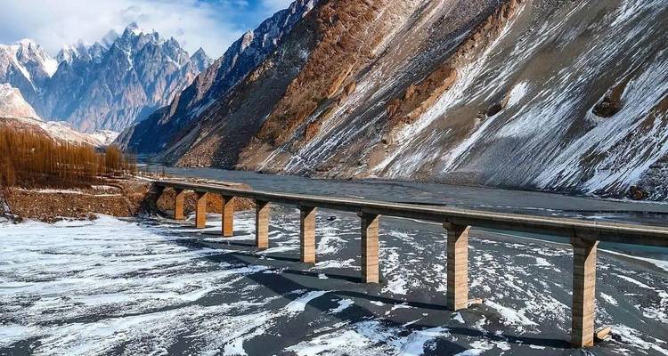 Long pont de béton enjambant une rivière glacée dans une gorge de montagne escarpée bordée de neige