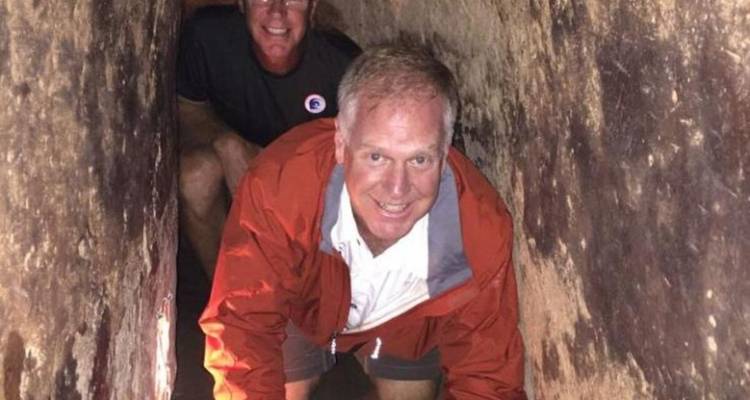 Two men crawling through a narrow underground tunnel.