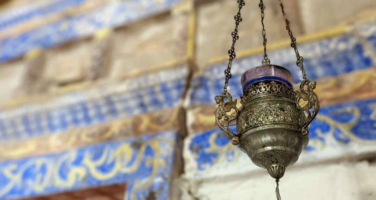 Sierlijke hangende metalen lamp met blauw glasdetail tegen kleurrijk beschilderde stenen muren.