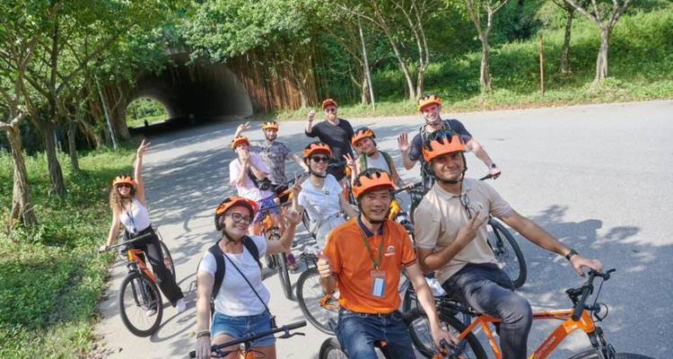 Groep fietsers met helmen die poseren voor een foto op een weg.